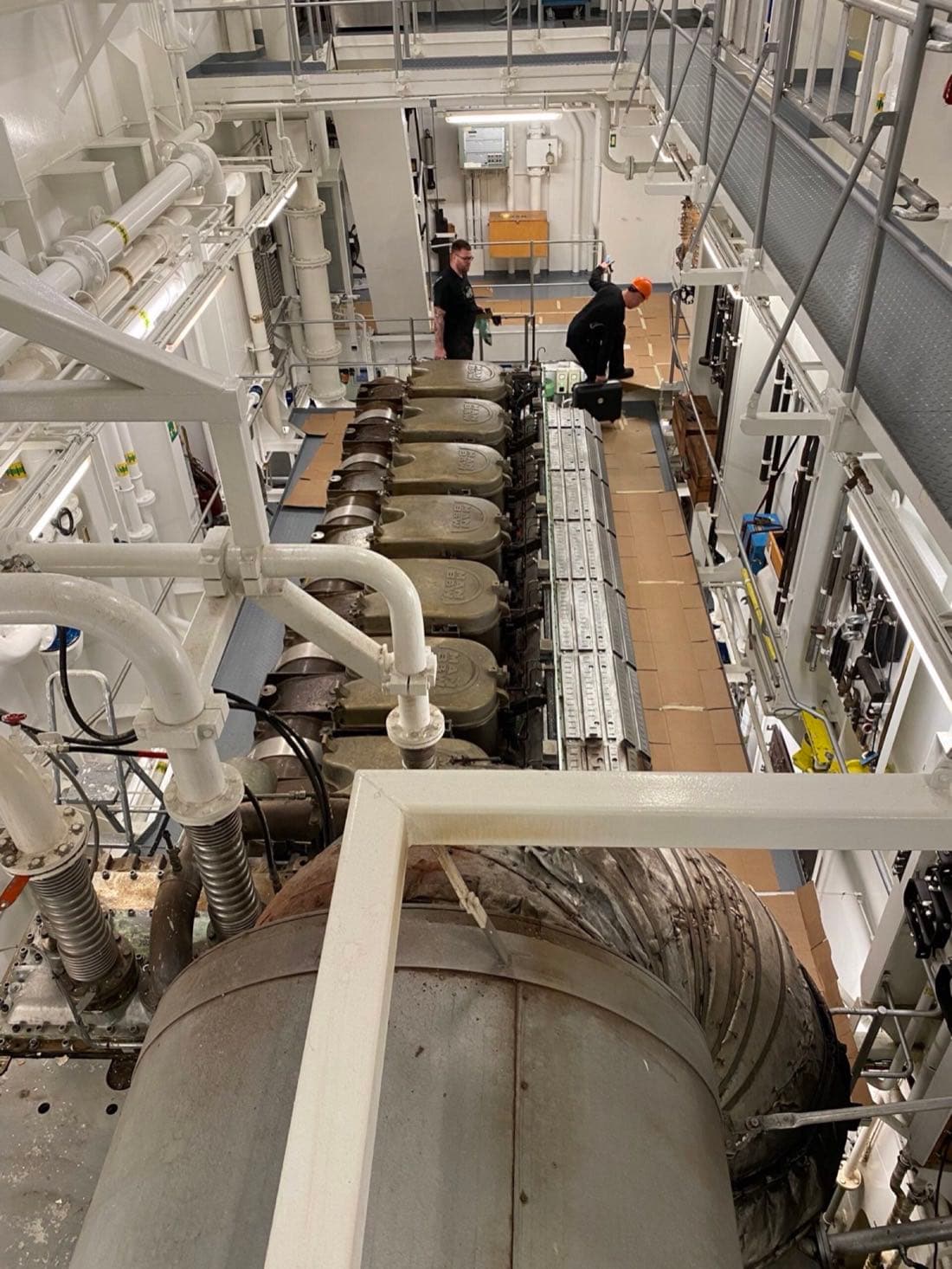Two engineers working on a main engine in a ship's engine room